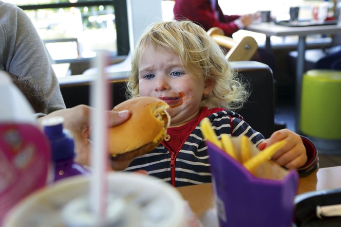 Upset toddler being given burger in fast food restaurant